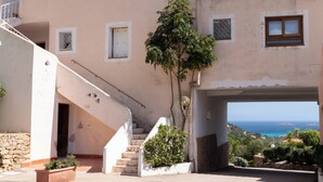 Un edificio de varios pisos con una escalera que lleva a un balcón, un árbol en una maceta y vistas al mar.