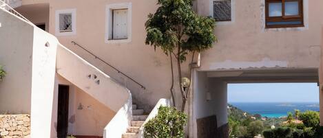 Un edificio de varios pisos con una escalera que lleva a un balcón, un árbol en una maceta y vistas al mar.