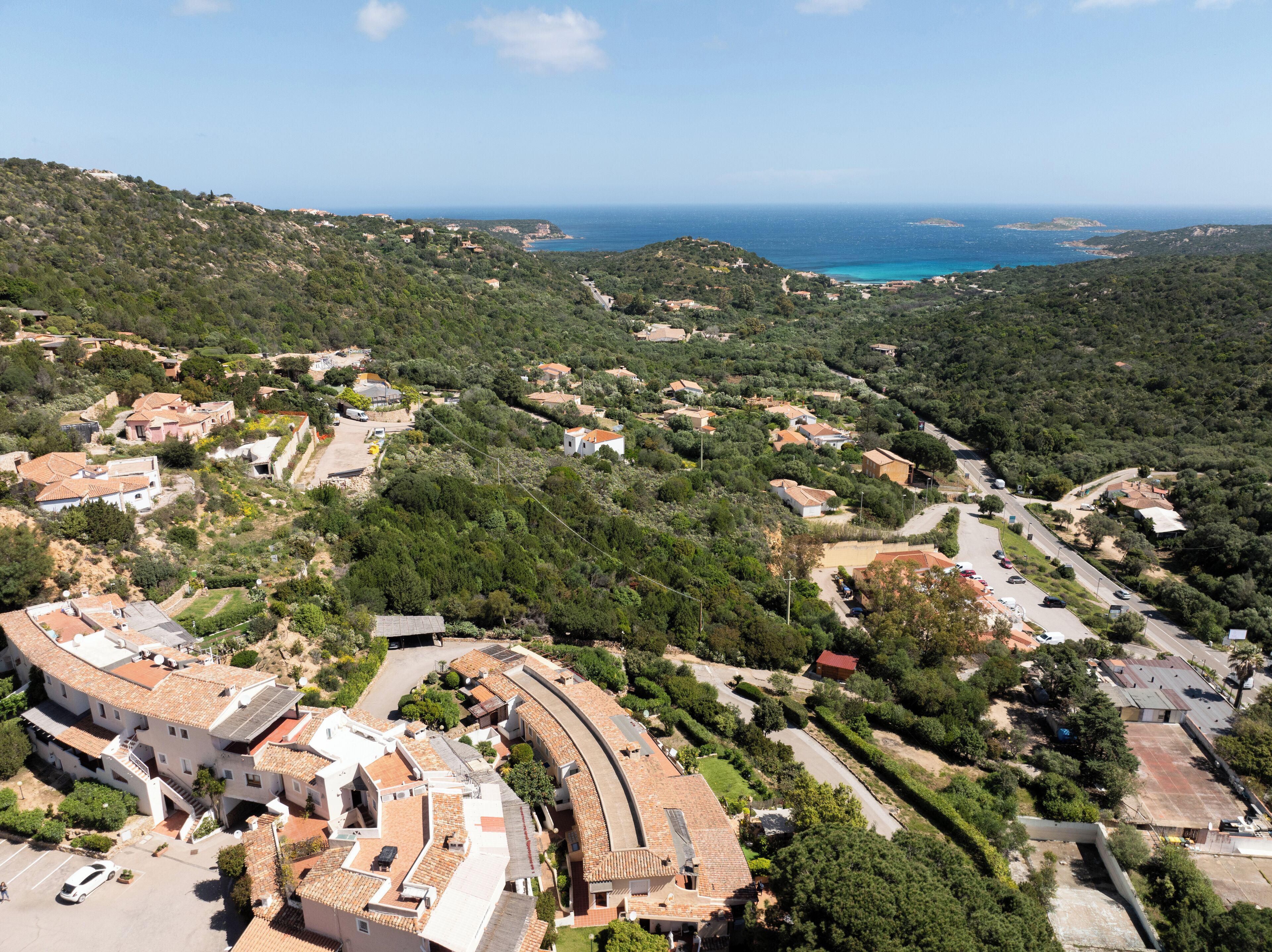 An aerial view of a coastal village with terraced houses, winding roads, and a view of the sea.