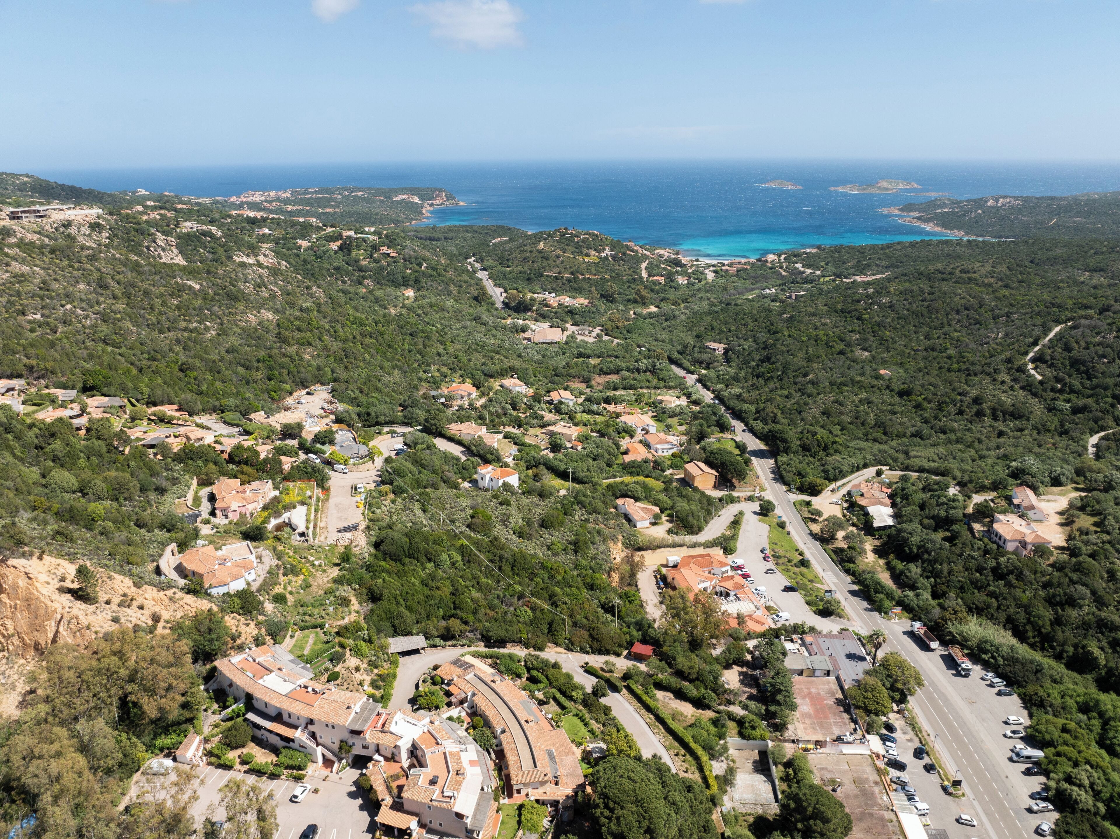An aerial view of a coastal village with terraced houses, a main road, and a clear view of the sea.