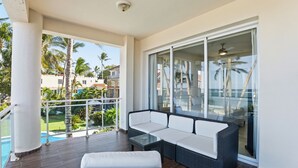 A balcony with a wicker sofa, a glass table, and a view of a swimming pool and palm trees. - Kite Beach Oceanfront condo  Hot tub and Pool 204 (Kite Beach)