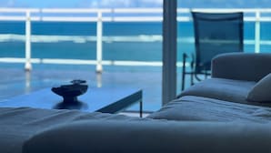 A modern room with a large window overlooking a balcony and the sea. There is a sofa and a small table with a decorative item on it. - Kite Beach Oceanfront condo  Hot tub and Pool 204 (Kite Beach)