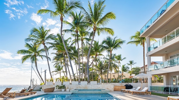 A pool area with lounge chairs and palm trees, overlooking a body of water. - Kite Beach Oceanfront condo  Hot tub and Pool 204 (Kite Beach)