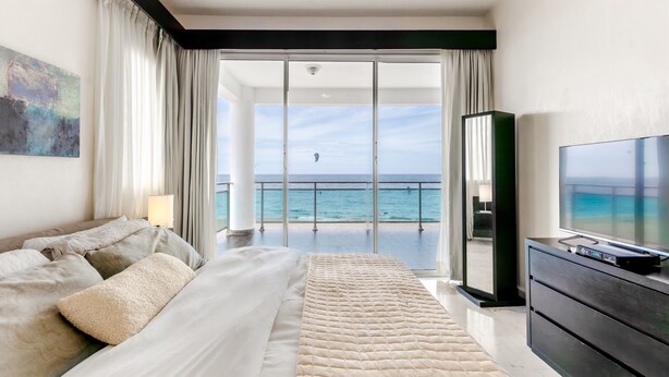 Quarto com uma cama grande, televisão e vista para o oceano.