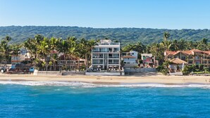 Um hotel à beira-mar com vários edifícios, palmeiras e vista para o oceano.