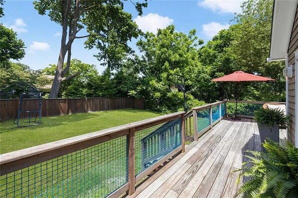 A wooden deck with a metal fence, a red umbrella, and a grassy yard with trees.