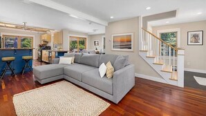 A modern living room with a grey sectional sofa, a patterned rug, and a staircase leading to an upper floor.