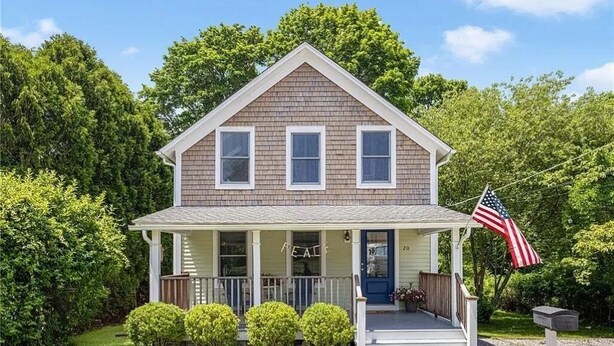 A two-story house with a front porch, a mailbox, and an American flag.