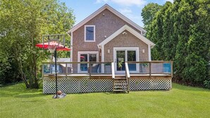 A two-story house with a deck, a basketball hoop, and a red umbrella.
