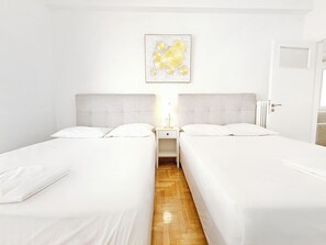 Ein Hotelzimmer mit zwei Betten, einem Nachttisch mit Lampe, einem gerahmten Bild an der Wand und einer Tür rechts.