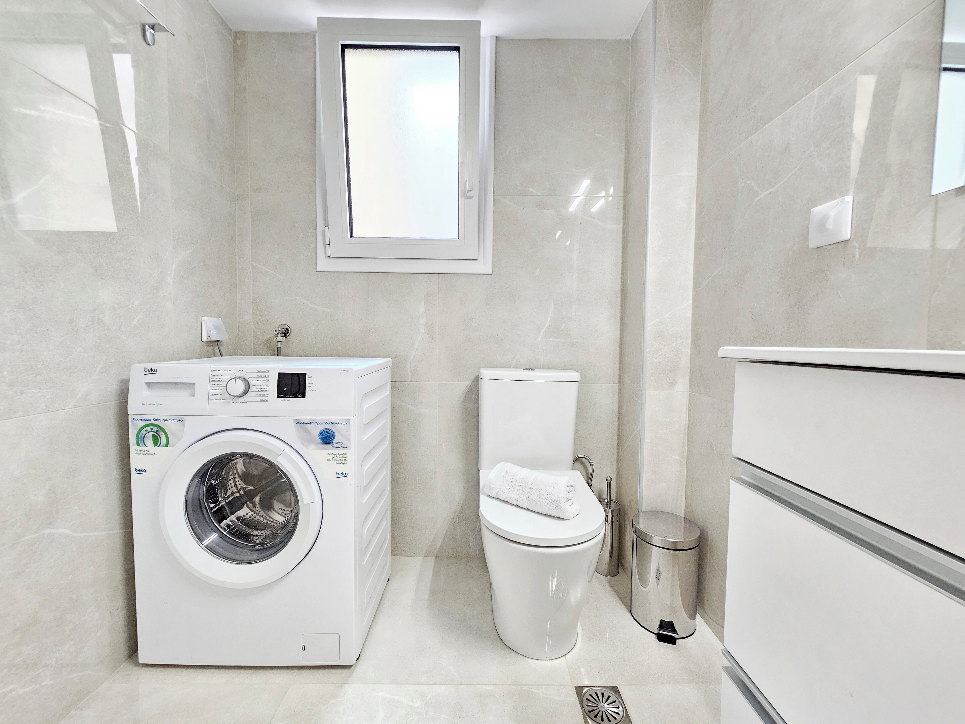 A modern bathroom with a built-in washing machine, toilet, and a small window.