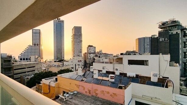 A cityscape at sunset with modern buildings, including a tall skyscraper and a building labeled "BY 14". - Ben Yehouda Obsidian (Tel Aviv)