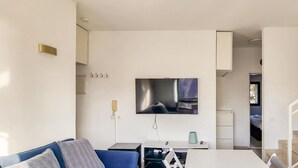 A modern living room with a flat-screen TV mounted on the wall, a sofa, a small table, and a staircase leading to another room. - Ben Yehouda Obsidian (Tel Aviv)