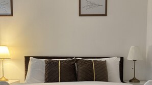 A neatly made bed with white and brown linens, two pillows, and a brown throw blanket. There are two lamps on either side of the bed.