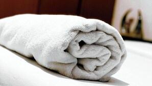 A neatly rolled white towel on a bed in a hotel room. - Rubee Homes (Kampala)