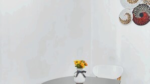 A dining area with a round table, two white chairs, and a vase with flowers. - Rubee Homes (Kampala)