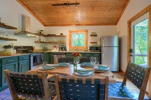 Une cuisine moderne avec un plafond en bois, des comptoirs en granit et un coin repas comprenant une table et des chaises en bois.