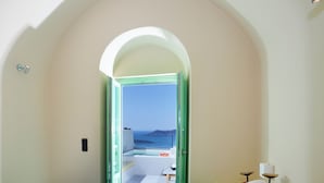 Un dormitorio con cama, puerta con marco verde que da a un balcón con vistas al mar.