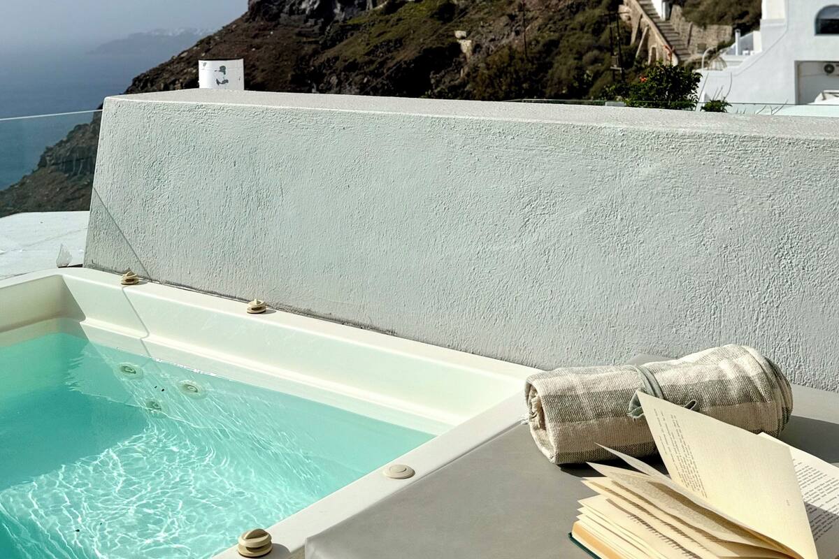 A pool area with a view of white buildings on a hillside and the ocean in the background.
