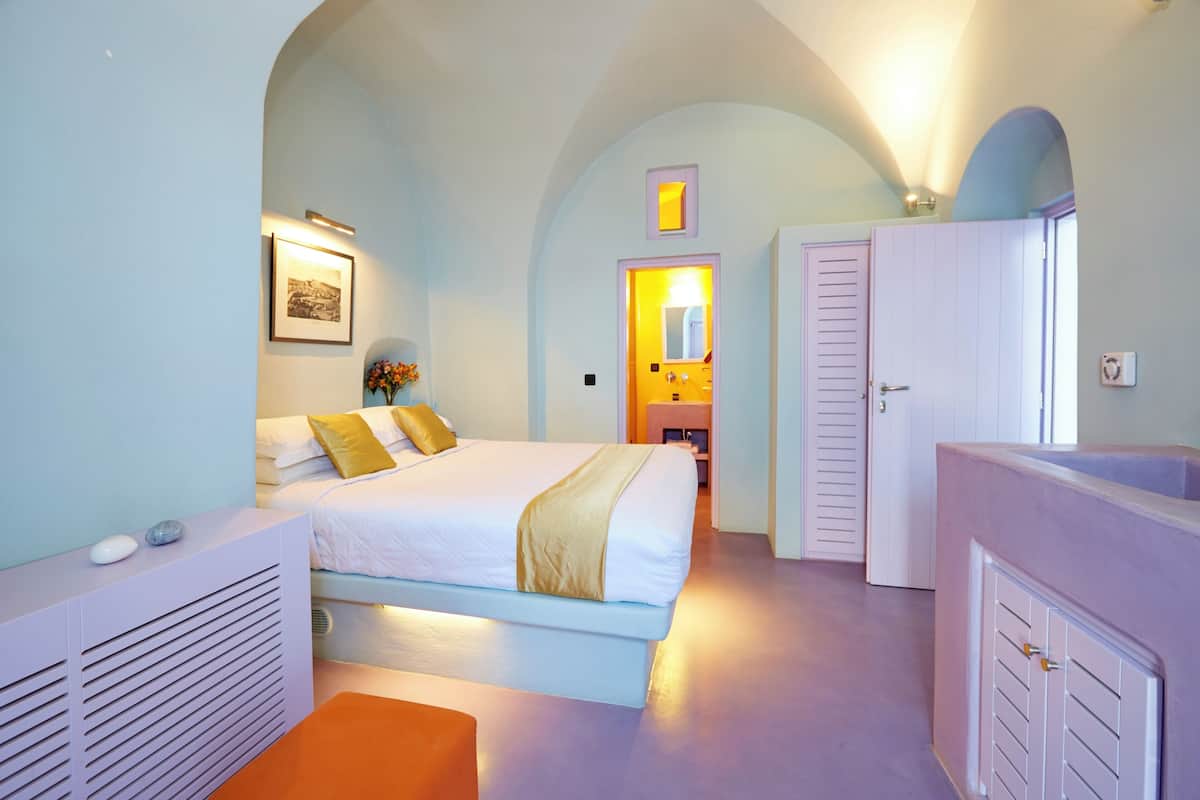 A bedroom with a bed, a bedside table, a mirror, and a door leading to another room.