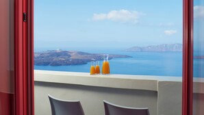 Un balcón con dos sillas y tres botellas de jugo de naranja, con vista a un paisaje marino y terreno distante.