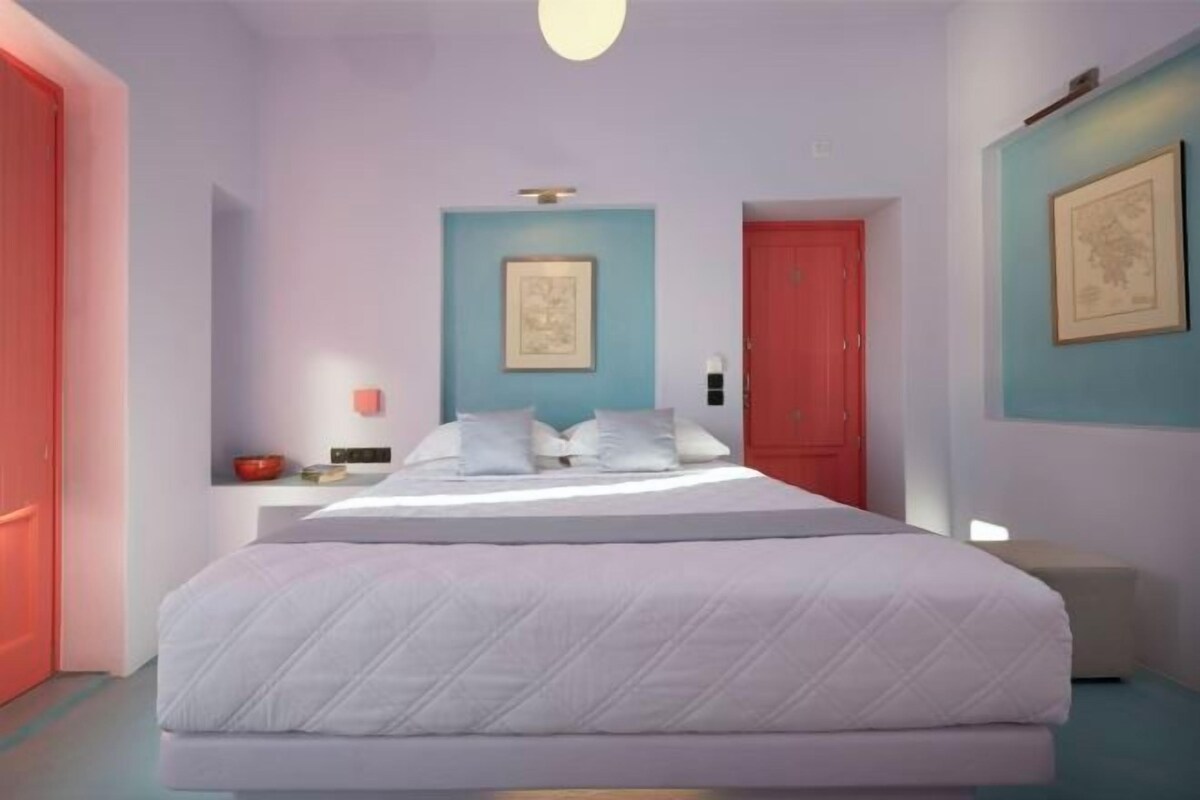 A bedroom with a bed, a nightstand, a red door, and a framed picture on the wall.