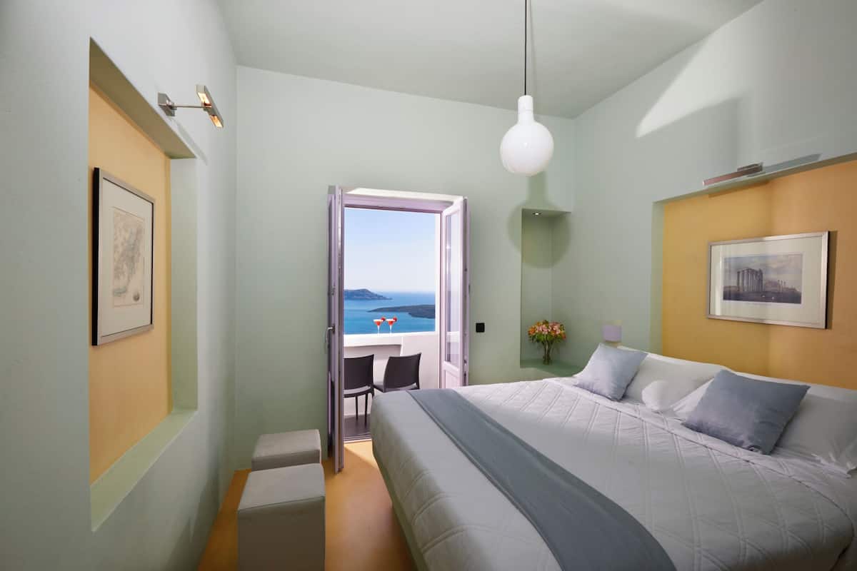 A bedroom with a bed, a desk with a chair, and a view of the sea.
