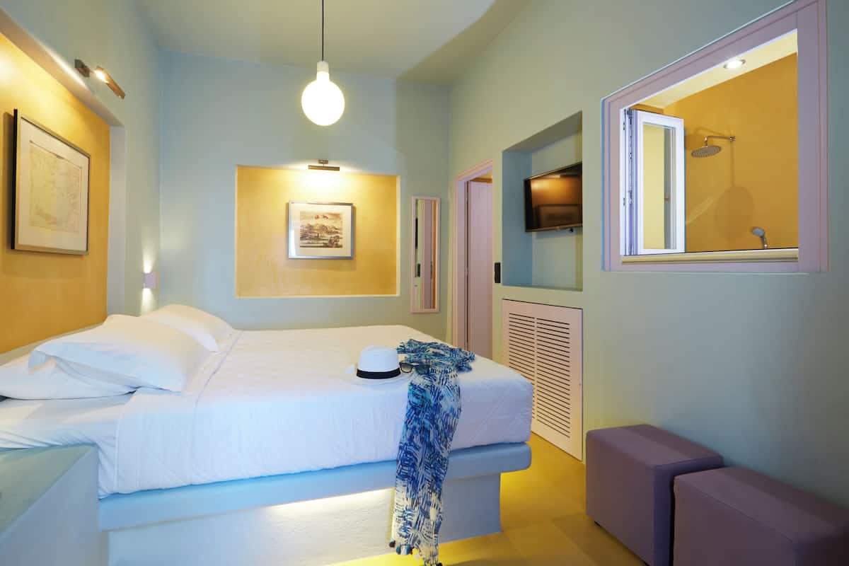 A bedroom with a bed, a bedside table, a hanging light fixture, a wall-mounted TV, and a bathroom with a shower.