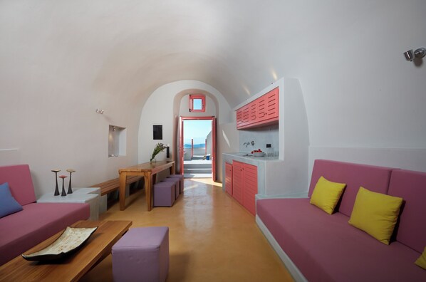 A compact living space with a pink sofa, a wooden table, and a kitchen area with pink cabinets.