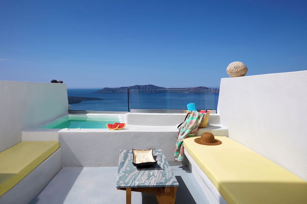 A sunlit terrace with a view of the sea, a small table, a bench, and a bathtub.