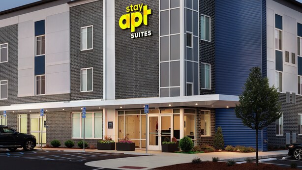 A modern hotel with a 'Stay Apt Suites' sign, featuring a brick facade, large windows, and a parking lot. - stayAPT Suites North Little Rock (North Little Rock)
