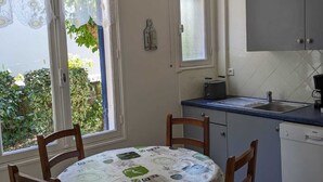 Una piccola cucina con un tavolo rotondo, sedie, una finestra con tende, un armadietto e un pavimento piastrellato.