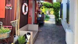 Un stretto vicolo con un edificio rosso da un lato e uno bianco dall'altro. Sono presenti aree con tavoli e sedie all'aperto e un gatto è seduto su un fioriere.