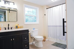 Een badkamer met een wit toilet, zwarte kastjes, een grote spiegel en een raam.