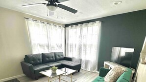A living room with a dark green sofa, a black leather couch, a coffee table, and a ceiling fan. - Charming 3-bedroom house in enjoyable Endwell (Endicott)