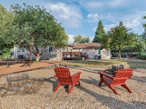 A house with a gravel patio, two Adirondack chairs, a wooden barrel, and a fire pit.