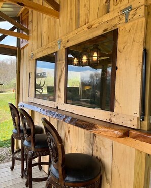 A wooden bar area with a view of the outdoors, featuring a wooden counter and three chairs. - Cozy cabin (New Lexington)