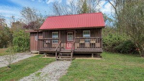 A wooden cabin with a red roof, a front porch with steps, and a gravel path leading to it. - Cozy cabin (New Lexington)