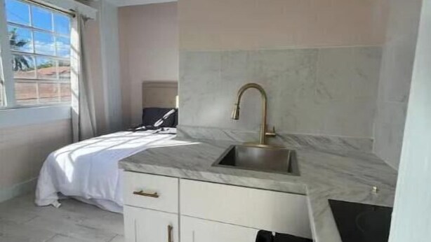 Une chambre d’hôtel de taille réduite, comprenant un lit, une petite kitchenette, une fenêtre avec des rideaux et un ventilateur de plafond.