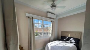 Une chambre à coucher avec un lit, un ventilateur de plafond, une fenêtre avec des rideaux et une vue sur l’extérieur.