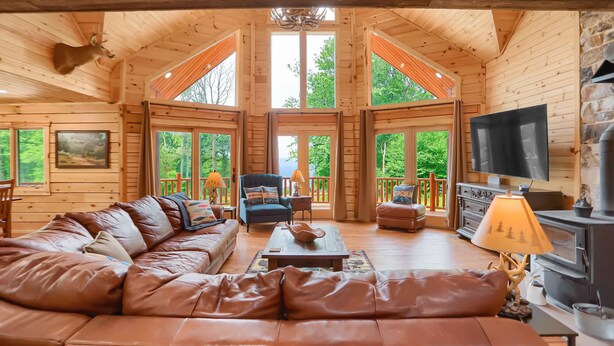 A cozy cabin interior with a leather sofa, a television, and a fireplace. - Eagle's Escape - Mountain top lodge with spectacular views (Huntingdon)