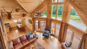 A wooden cabin interior with a loft bedroom, a dining area, and a living room with a leather sofa and a blue armchair. - Eagle's Escape - Mountain top lodge with spectacular views (Huntingdon)