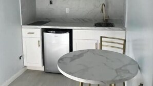 Een kleine keuken met witte kastjes, een magnetron, een spoelbak en een eettafeltje met stoelen.