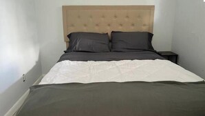 Een bed met een gestoffeerd hoofdbord, twee donkere kussens en een witgroene dekbedovertrek.