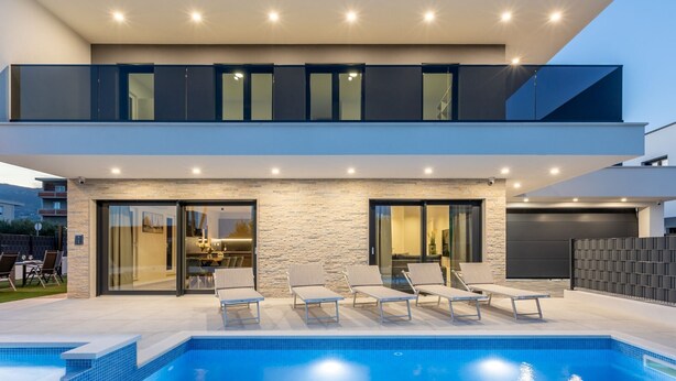 A modern two-story house with a swimming pool, outdoor seating, and a stone facade.