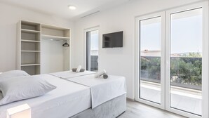A modern bedroom with two beds, a built-in wardrobe, a TV, and large windows offering a view of the city.