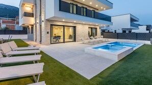 A modern two-story house with a swimming pool, outdoor seating, and a stone facade.