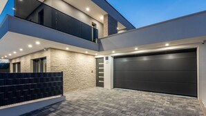 A modern two-story house with a large garage, stone facade, and a paved driveway.
