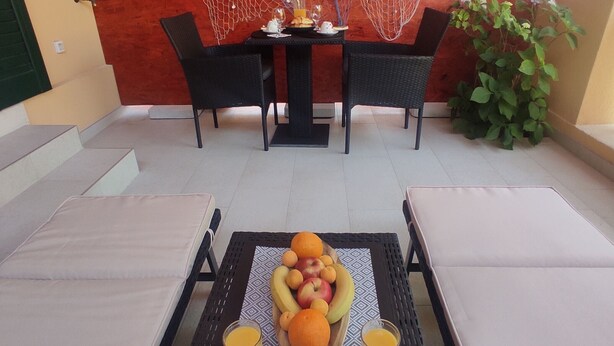 Un coin repas avec une table dressée pour deux personnes, agrémenté d’un panier de fruits et de deux verres de jus d’orange.