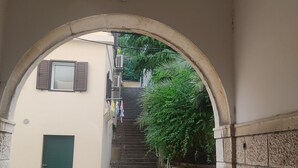 Une ruelle étroite avec une porte verte, une petite fenêtre avec des volets et un escalier menant à un niveau supérieur.